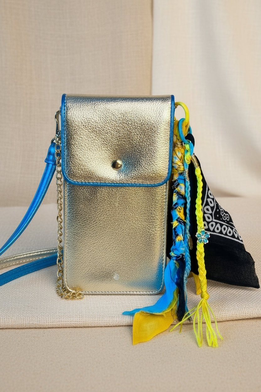 Le Grigri de sac Bandana Miya accroché à une petite pochette dorée à bandoulière bleue, illustrant comment cet accessoire personnalise et dynamise un sac de soirée. Joyas by jo