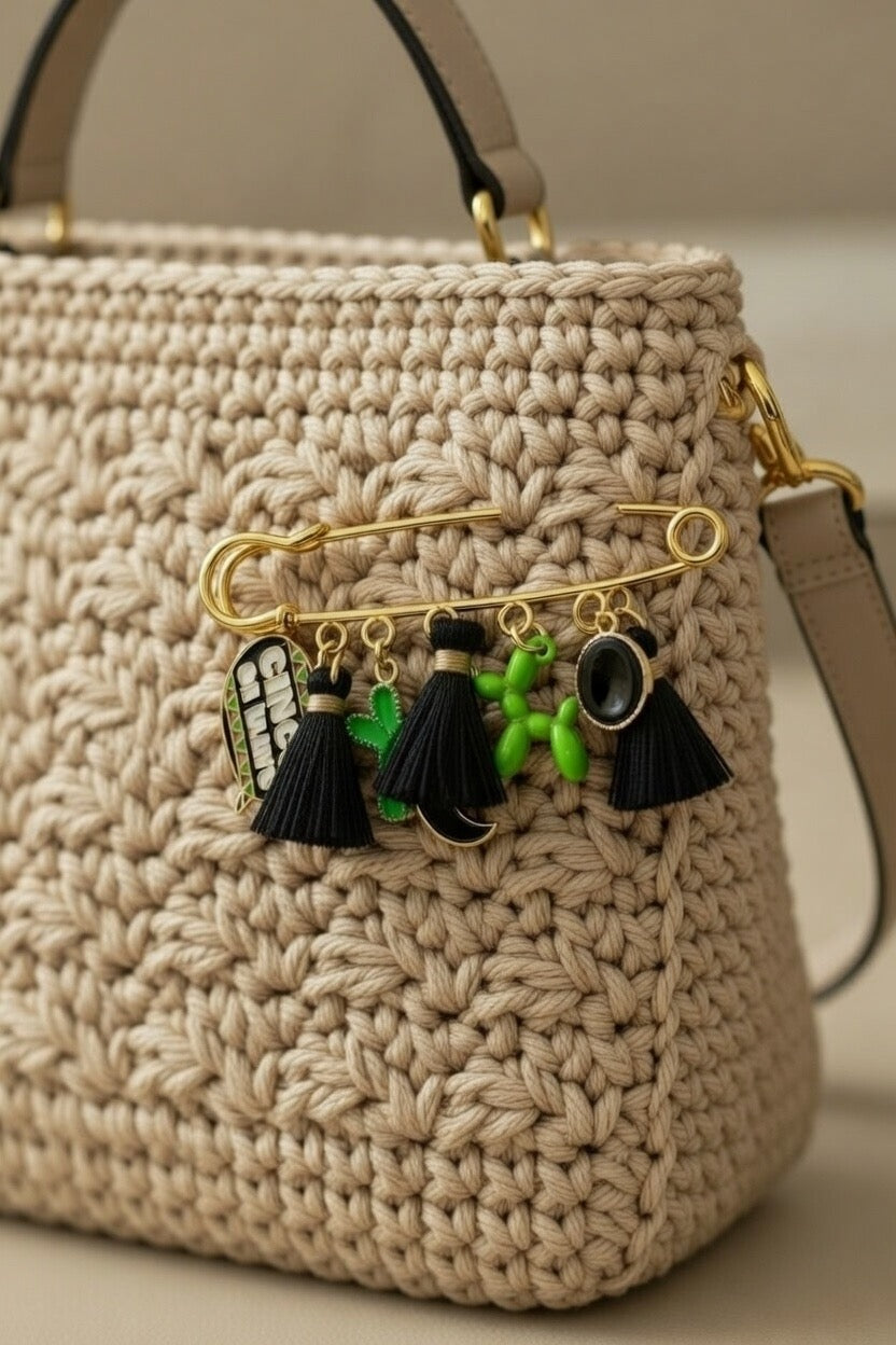 Sac à main artisanal en crochet beige avec bijou de sac amovible. Épingle dorée à breloques noires et vertes pour une personnalisation élégante et moderne d'accessoires faits-main.