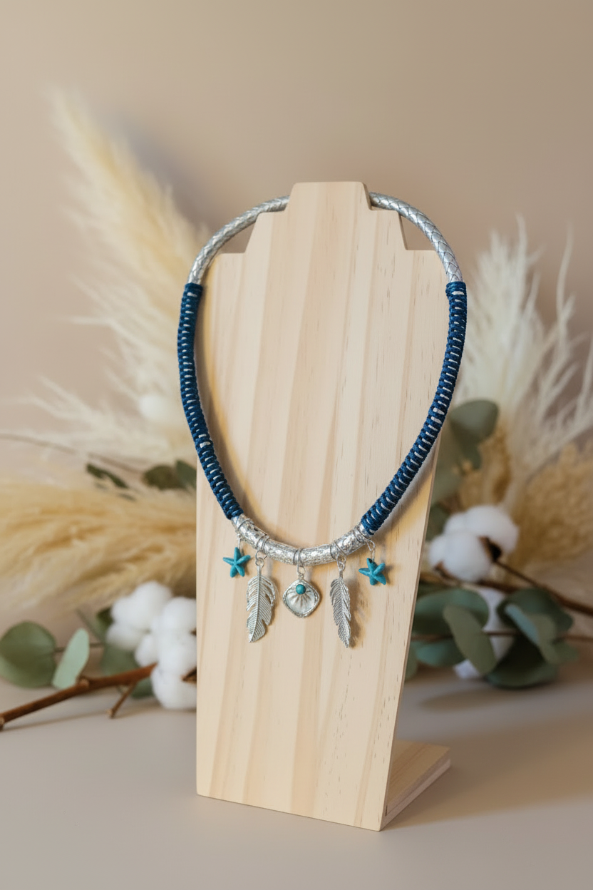 Présentation complète du collier artisanal Joyas by Jo avec cordon bleu et argent, plumes et perles turquoises sur fond décoratif naturel.