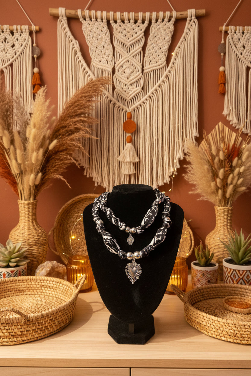 Collier double en tissu à motifs noir et blanc exposé dans un décor naturel avec macramé, paniers en osier et fleurs séchées.