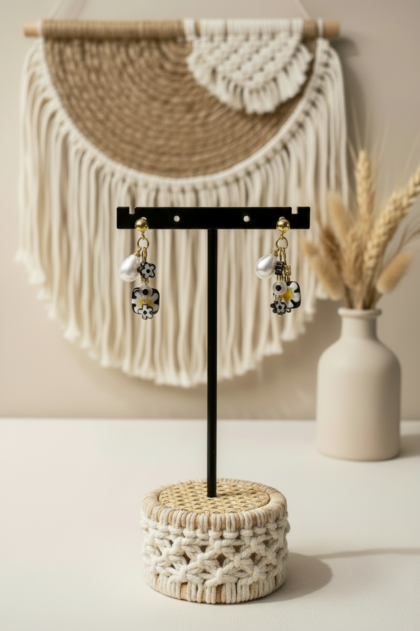 Boucles d'oreilles pendantes Joyas by Jo avec perles baroques blanches et fleurs en résine noir et blanc, présentées sur un support en macramé dans un décor bohème chic.