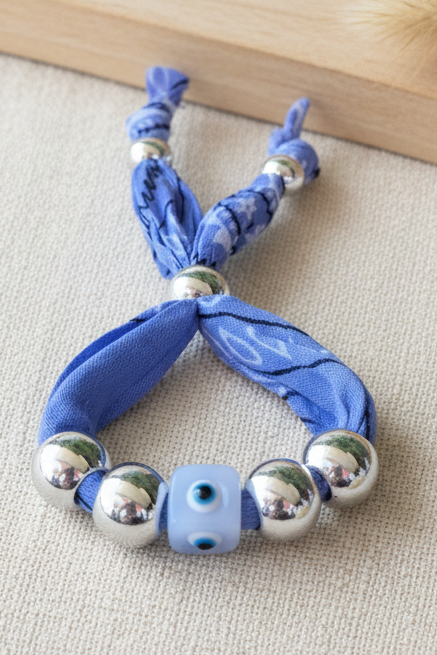 Vue détaillée du bracelet Alisa "Aura Protectrice" réalisé en tissu bandana bleu avec une perle centrale œil bleu et des billes argentées.Joyas by jo