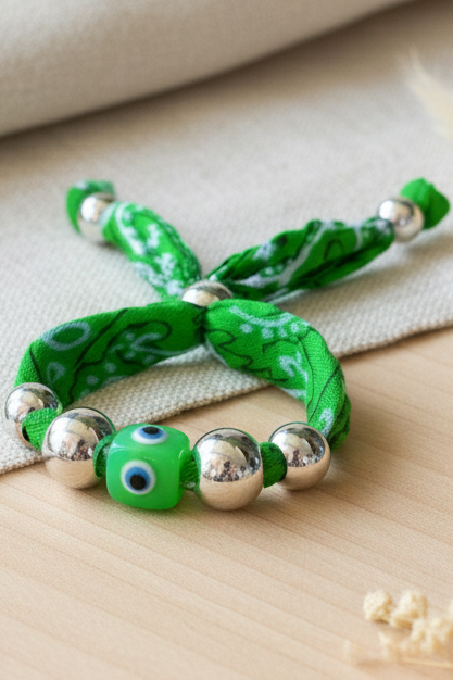 Vue détaillée du bracelet Karina "Regard d'Émeraude" composé d'un cordon vert tressé, de perles argentées et d'une perle centrale œil protecteur, posé sur un support neutre. Joyas by jo