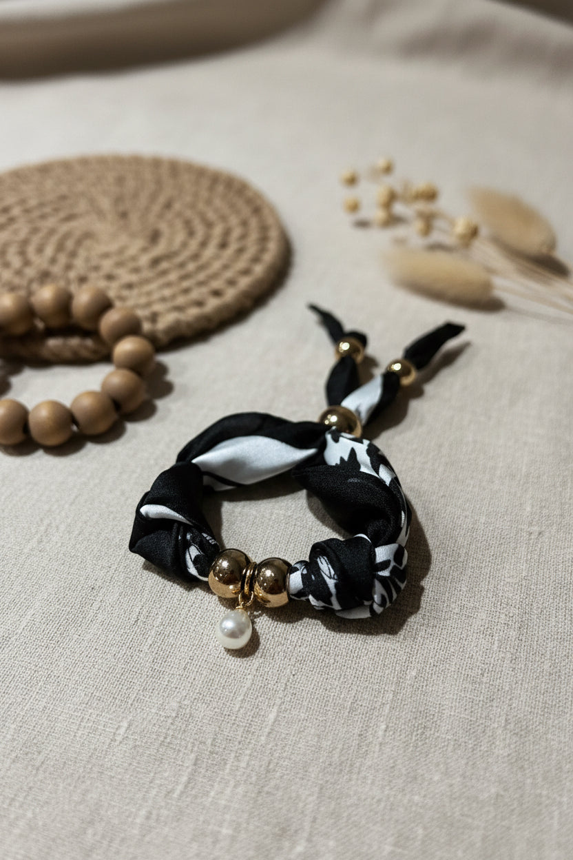 Bracelet Luna en tissu noir et blanc posé sur un linge en lin devant un macramé mural mural bohème.