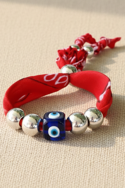 Bracelet Tessa "Passion" confectionné avec un tissu bandana rouge vif, agrémenté de perles argentées et d'une perle centrale en verre représentant un œil protecteur bleu. Joyas by jo