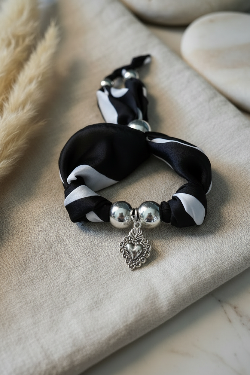 Bracelet Joyas by Jo en tissu noir et blanc avec perles argentées et pendentif coeur sacré sur fond lin.