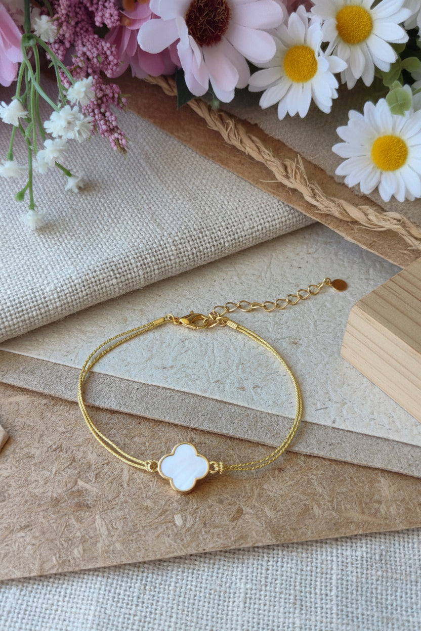 Bracelet fin en fil doré avec pendentif trèfle en nacre blanche, style minimaliste et bohème.