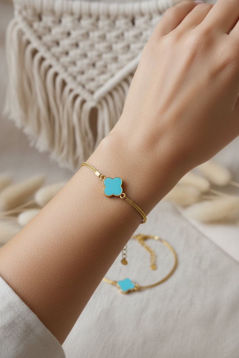 Bracelet fin en fil doré résistant porté au poignet, avec pendentif trèfle bleu turquoise, style bohème chic.