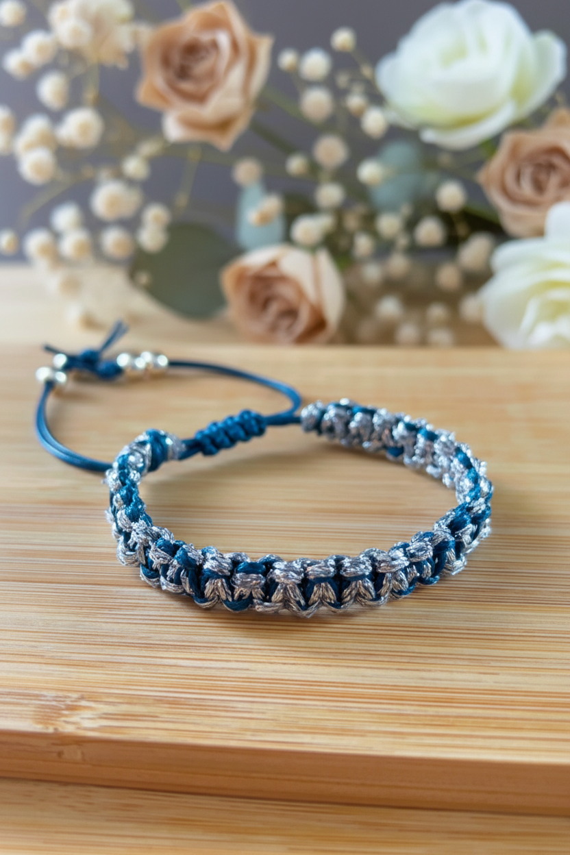 Gros plan d'un bracelet artisanal Joyas by Jo en cordon bleu et fils argentés sur un support en bois avec fleurs.