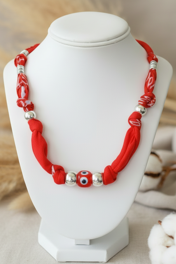 Collier Anna "Œil Protecteur" composé de perles rouges vibrantes et de perles argentées, avec une perle centrale en céramique représentant l'œil protecteur, exposé sur un buste blanc. Joyas by jo