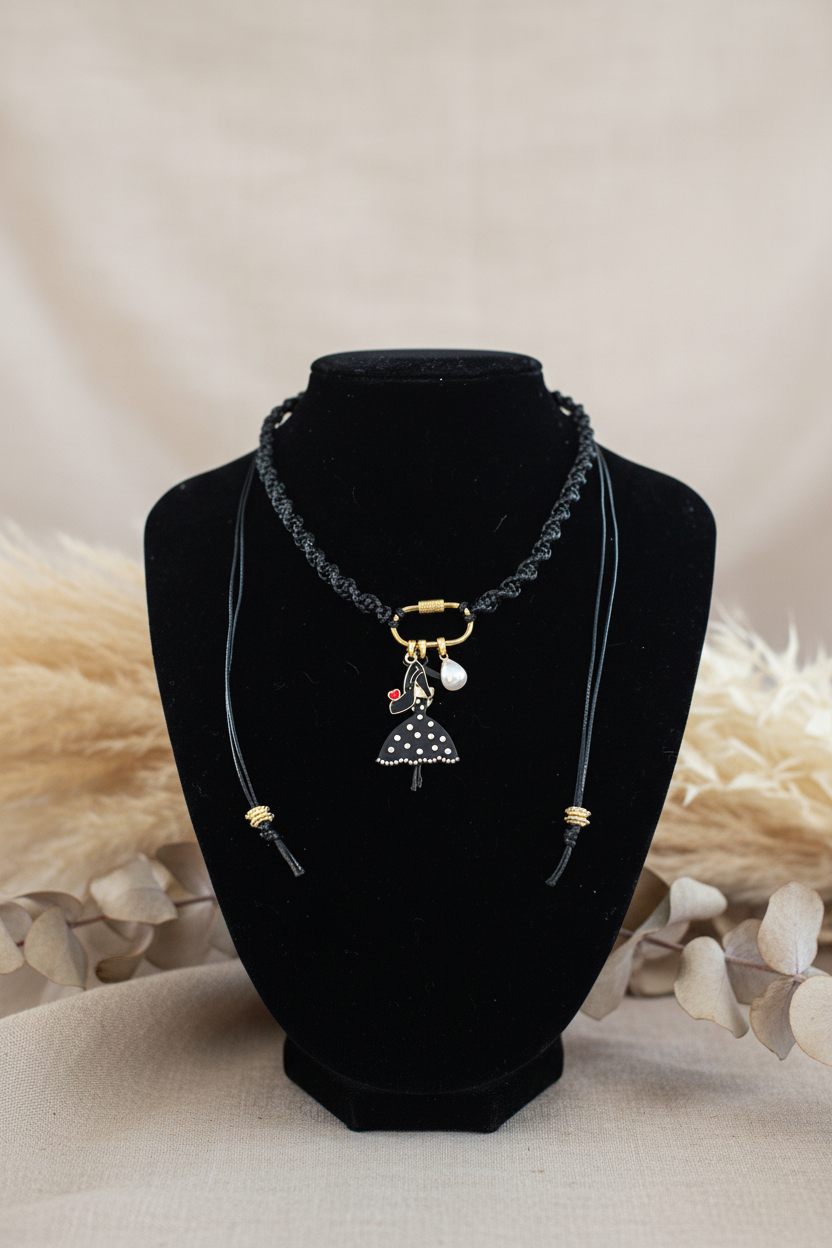 Collier artisanal Joyas by Jo avec cordon noir tressé et pendentif poupée à pois noirs et blancs sur un buste d'exposition.