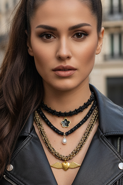 Gros plan sur femme de trois colliers artisanaux Joyas by Jo : perle, fleur noire et cœur doré ailé.