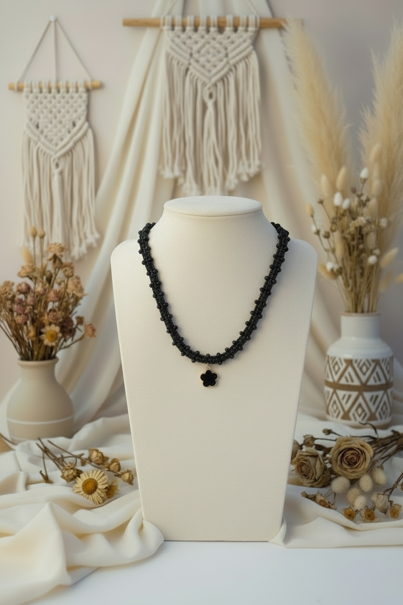 Collier noir artisanal Joyas by Jo avec pendentif fleur noire présenté sur un buste blanc décoratif.