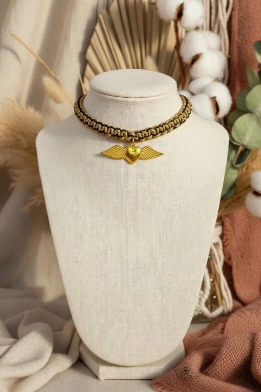 Collier ras du cou Joyas by Jo tressé noir et or avec pendentif cœur ailé doré présenté dans un décor bohème.