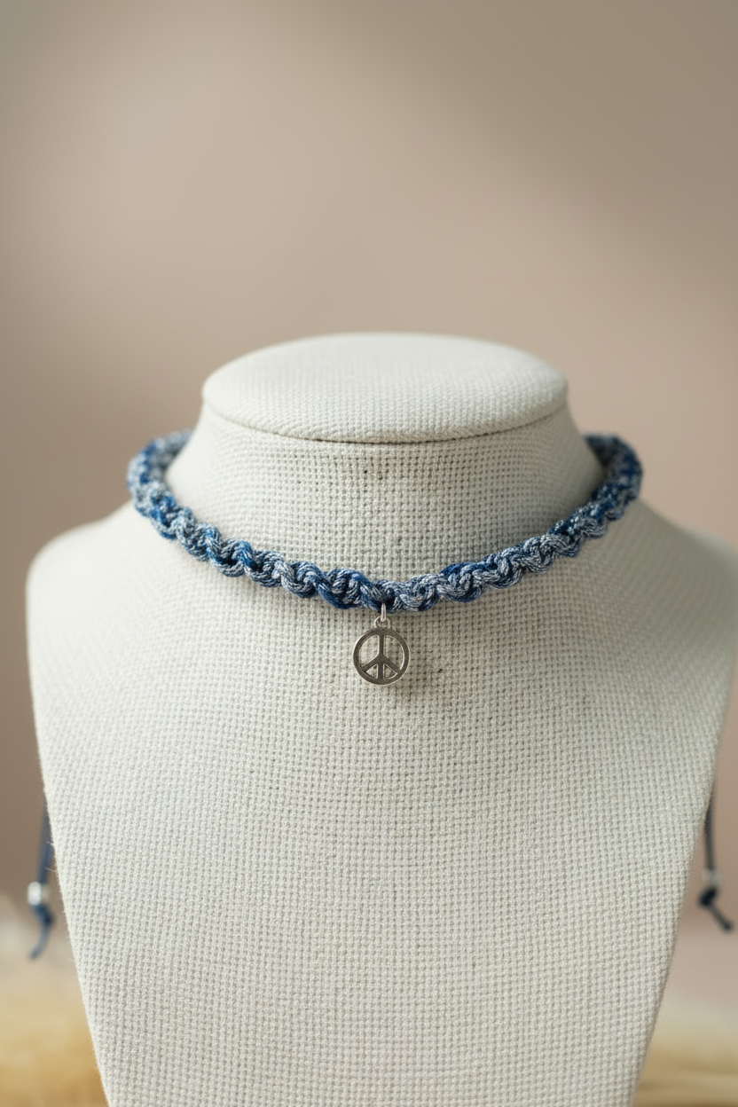 Détail du tressage artisanal d'un collier choker bleu chiné orné d'une médaille peace and love sur un buste de présentation blanc.