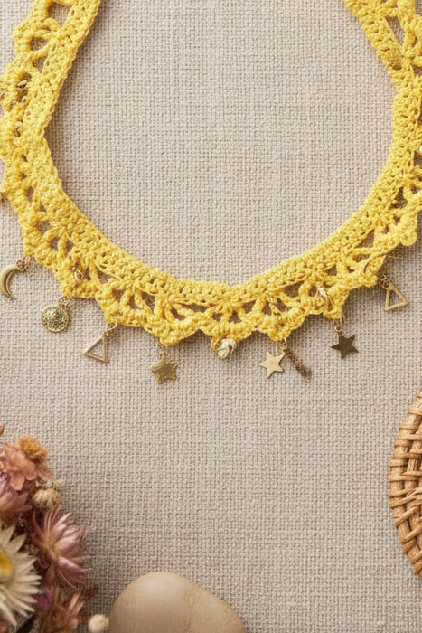 Détails des pampilles dorées en forme de lune et d'étoile sur la maille de coton jaune crochetée à la main.