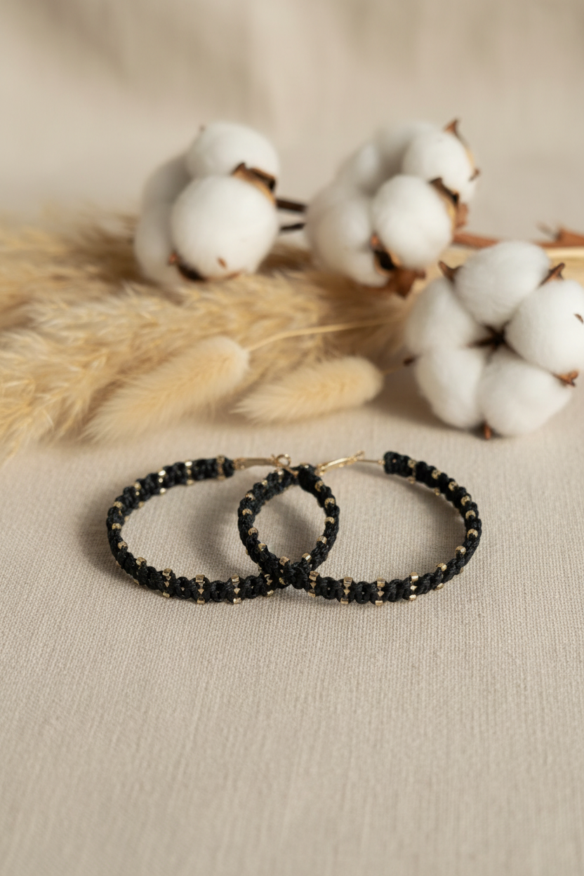 Gros plan sur les détails du tissage macramé noir et des perles dorées des boucles d'oreilles Joyas by Jo dans un décor bohème.