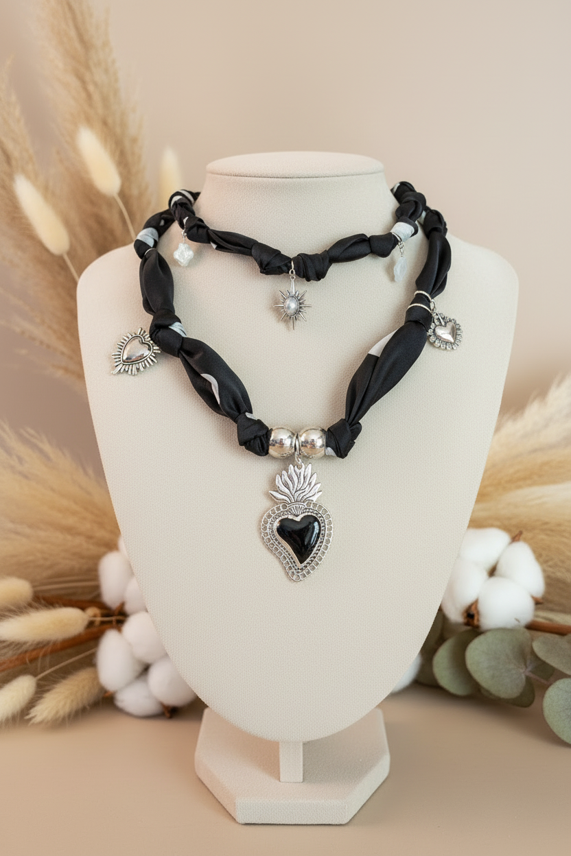 Accumulation de deux colliers Joyas by Jo en tissu noir avec pendentifs sacré cœur et soleil sur un buste entouré de fleurs de coton.