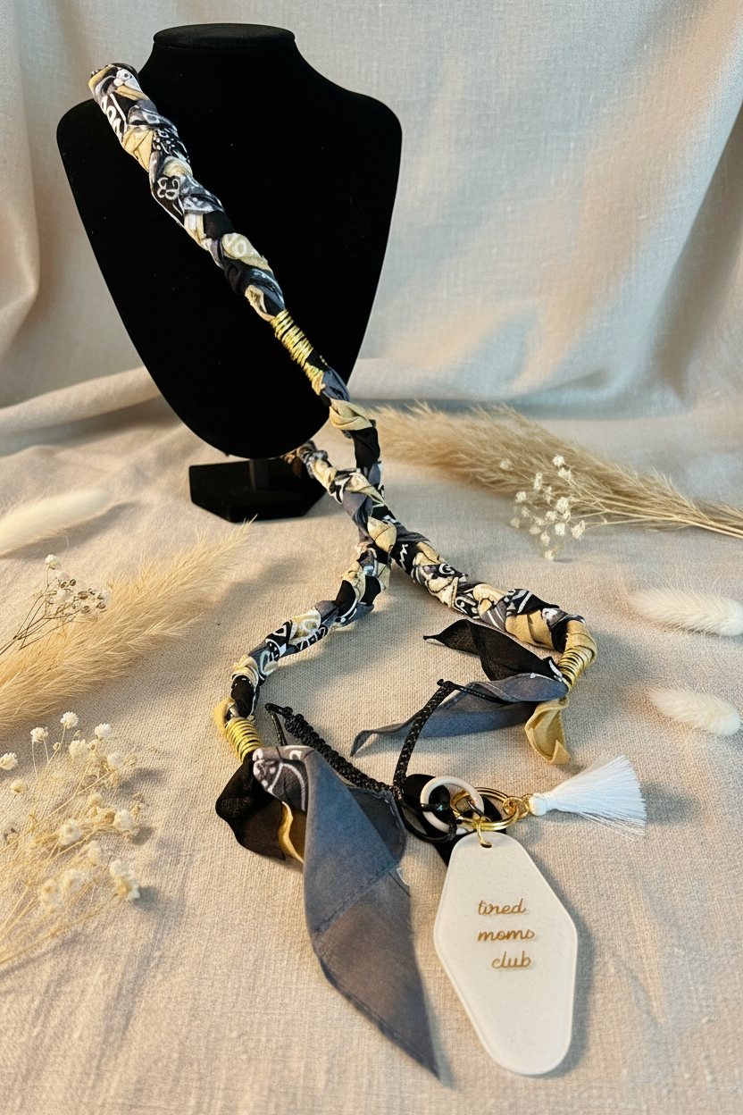 Collier de téléphone artisanal Joyas by Jo en tissu noir et doré avec pendentif blanc gravé Tired Moms Club.