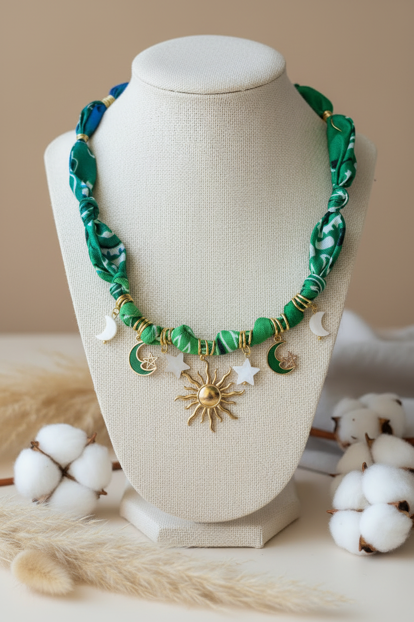Collier Joyas by Jo en tissu vert noué présenté sur un buste blanc, orné de pendentifs célestes : un grand soleil doré central, des croissants de lune et des étoiles nacrées.