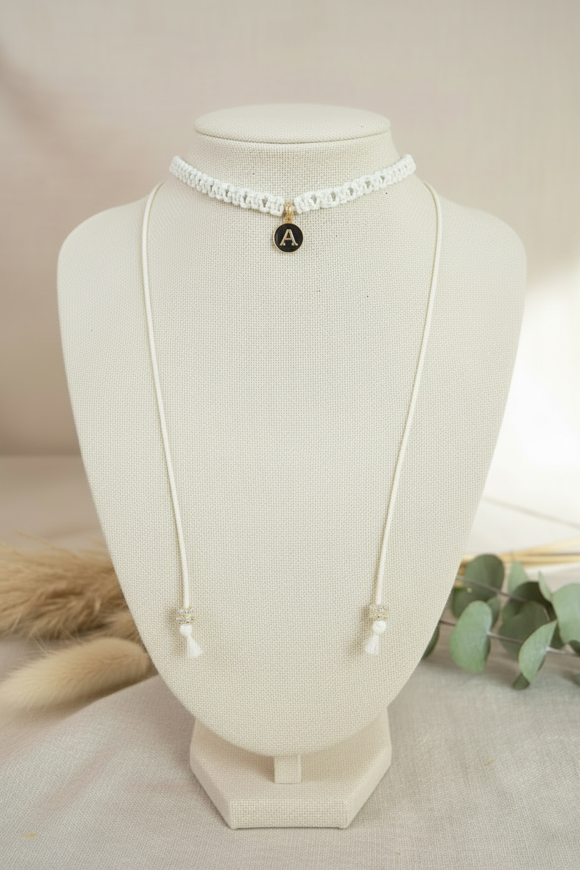 Collier choker blanc en maille tressée orné d'un pendentif noir avec l'initiale A dorée, présenté sur un buste d'exposition beige.