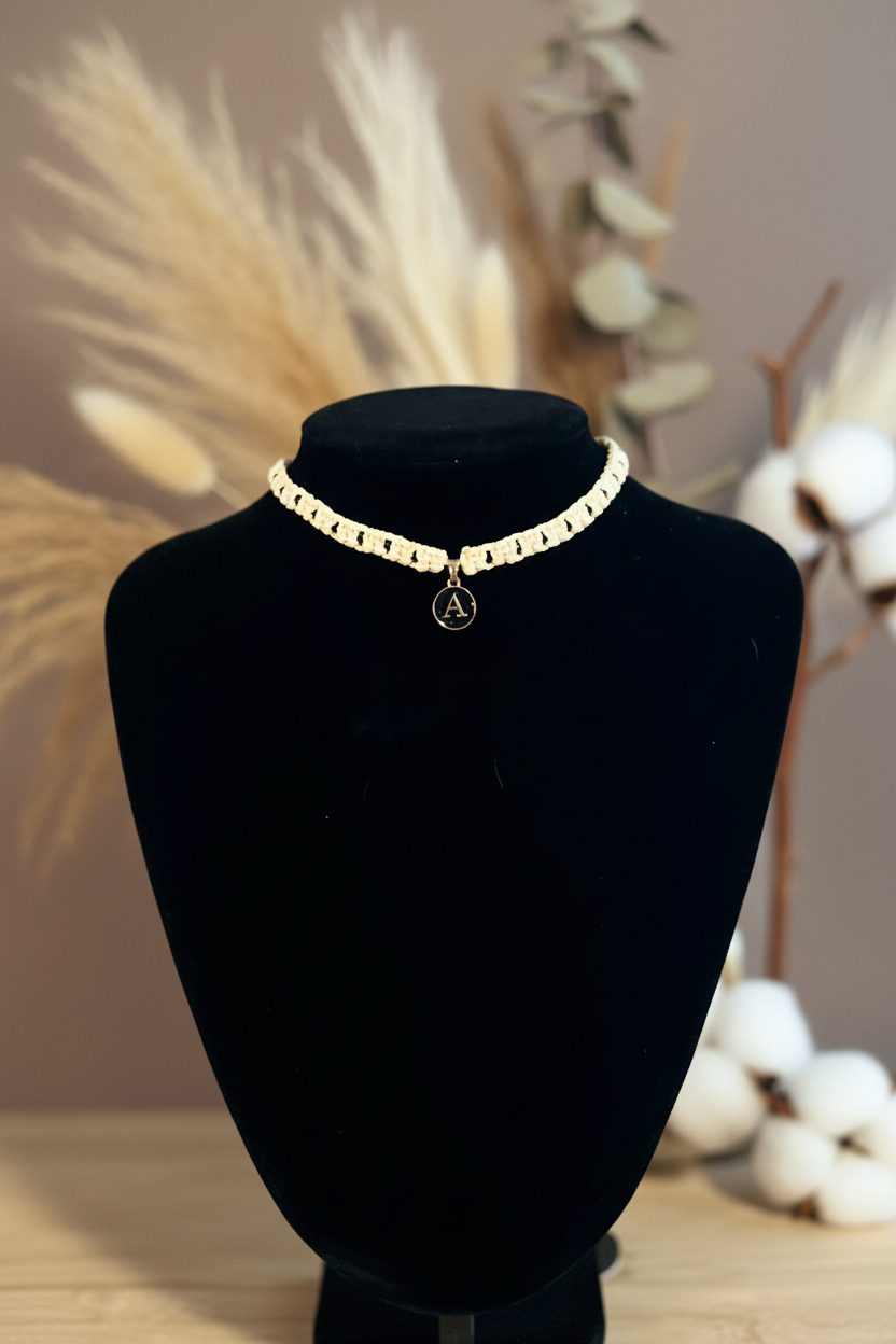 Collier ras de cou Joyas by Jo en macramé crème avec médaillon lettre A dorée sur buste noir.