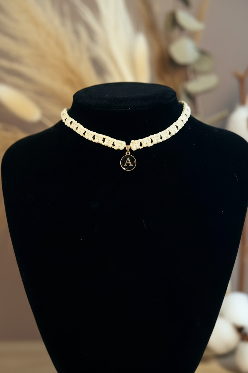 Gros plan du collier Joyas by Jo en fil tressé beige et perles marrons avec pendentif initiale A.