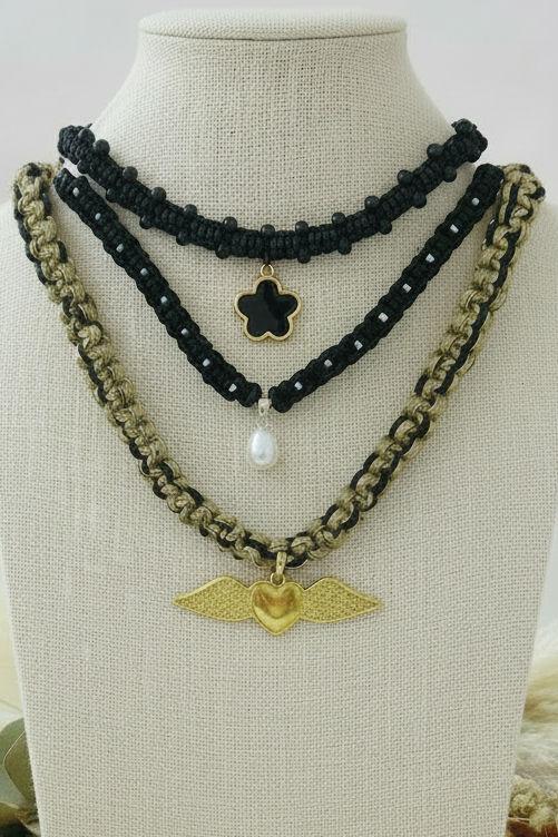 Gros plan sur buste de trois colliers artisanaux Joyas by Jo : perle, fleur noire et cœur doré ailé.