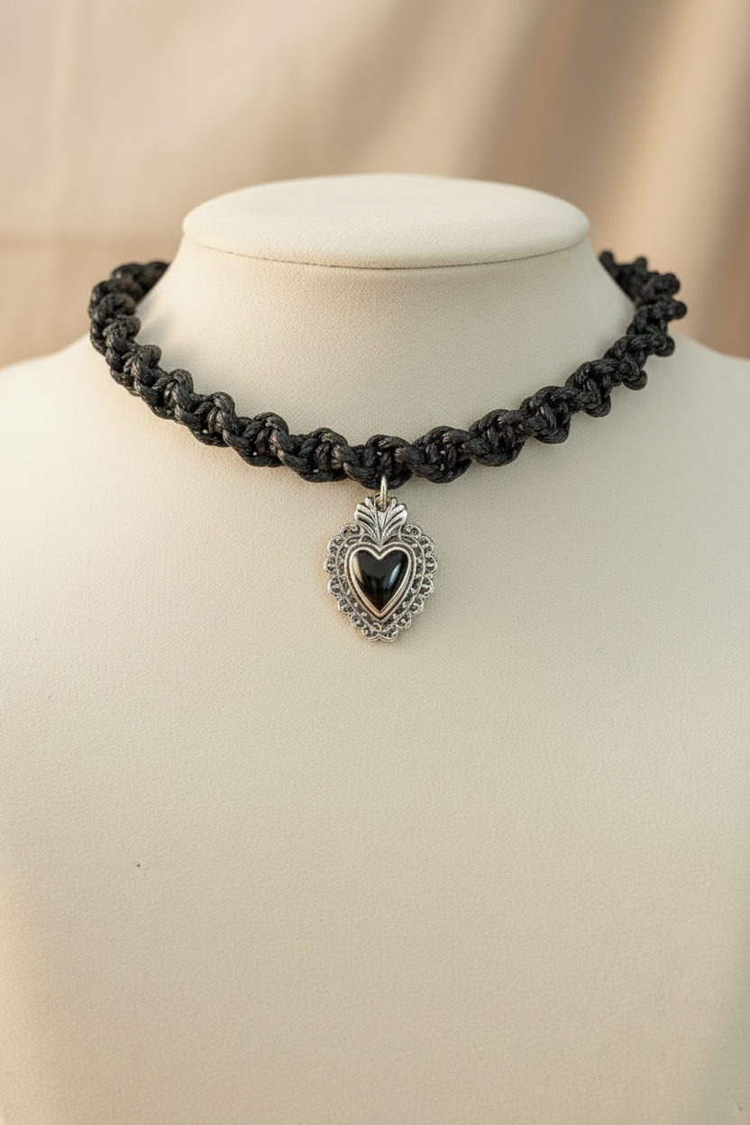 Gros plan d'un collier ras de cou artisanal noir Joyas by Jo orné d'un médaillon cœur en argent ciselé et pierre noire centrale.